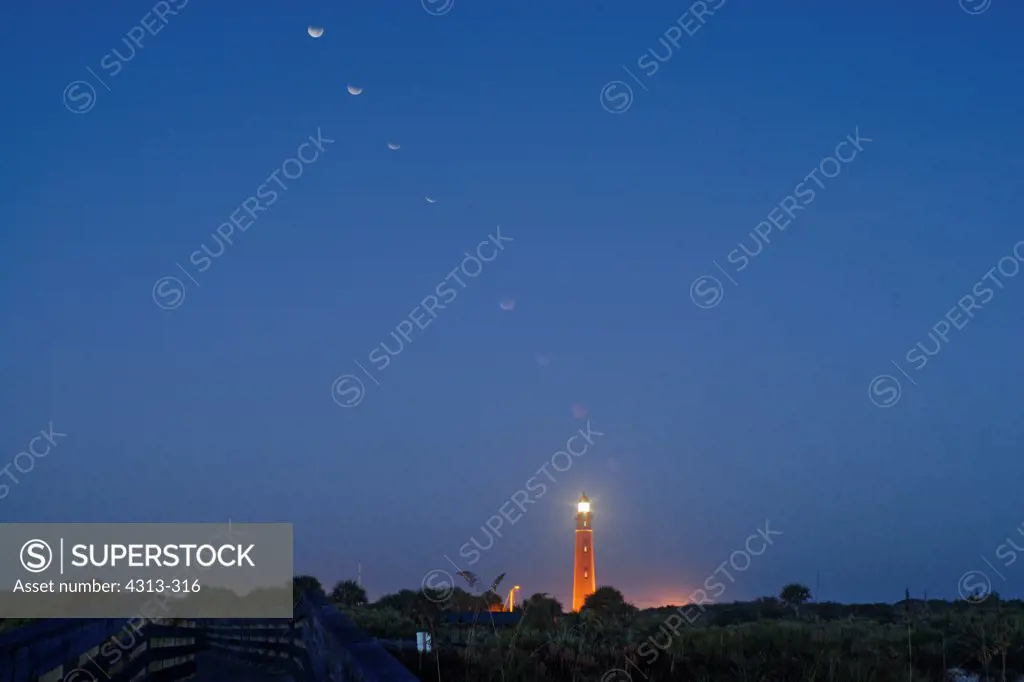 A multiple exposure captures the moon as it enters totality during the 2007 total lunar eclipse as seen over the Ponce de Leon Inlet lighthouse at sunrise