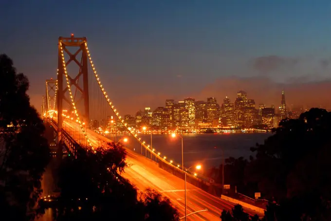 Bay Bridge lit up at dusk with skyline in the background seen from Yerba Buena Island, San Francisco Bay, San Francisco, California, USA