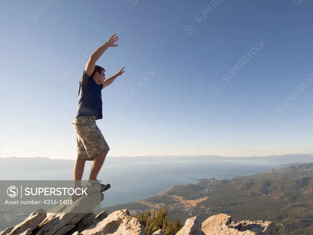 A Hiker Gazes Across Lake Tahoe at Sunset From a Mountaintop as He Leans Into the Wind