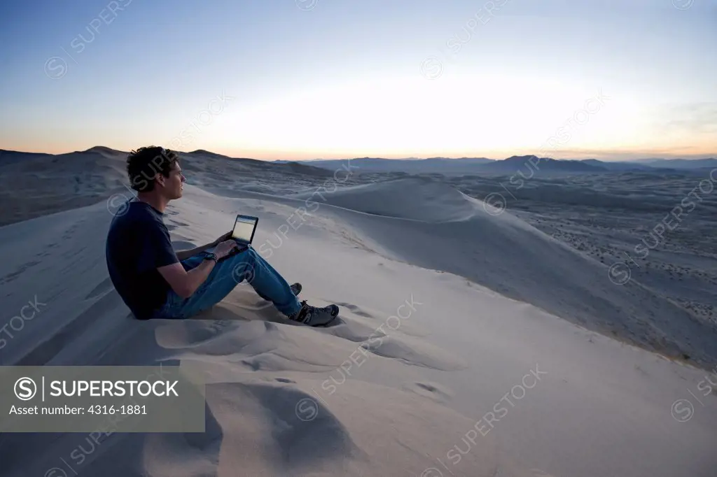Man Uses A Laptop On a Dune Field at Dusk