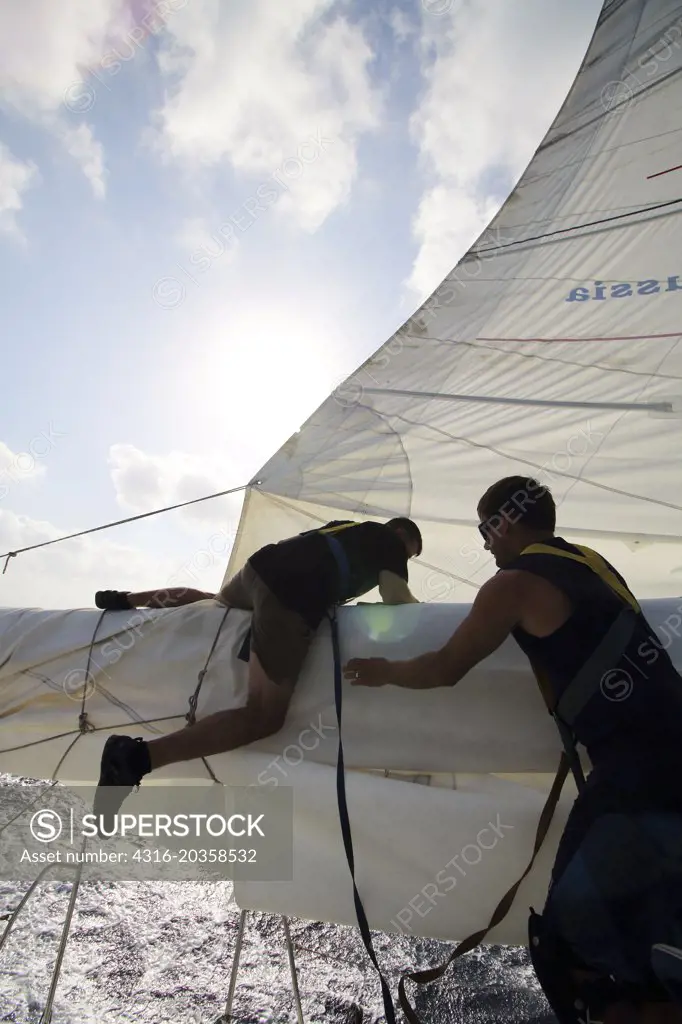 Sailor fixes torn sail on racing yacht as boat is in motion, South China Sea