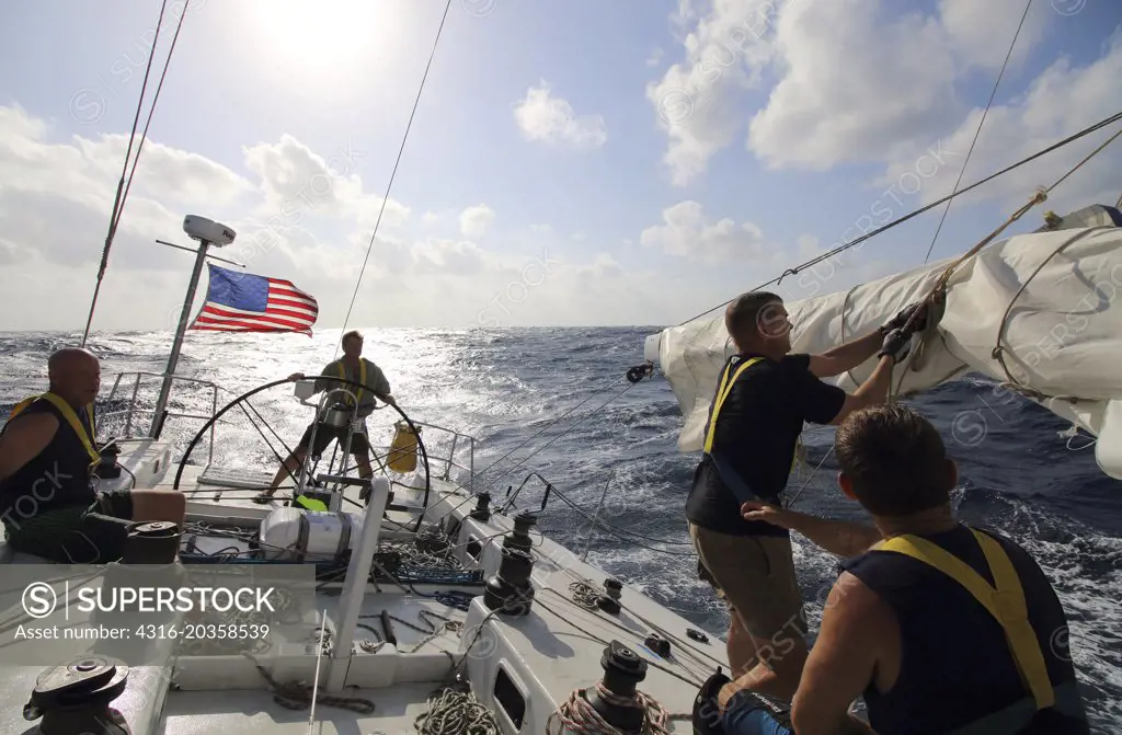Sailor fixes torn sail on racing yacht as boat is in motion, South China Sea