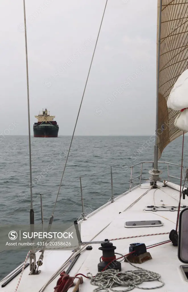 Large bulk cargo ship seen through the lines of a racing yacht, Strait of Malacca