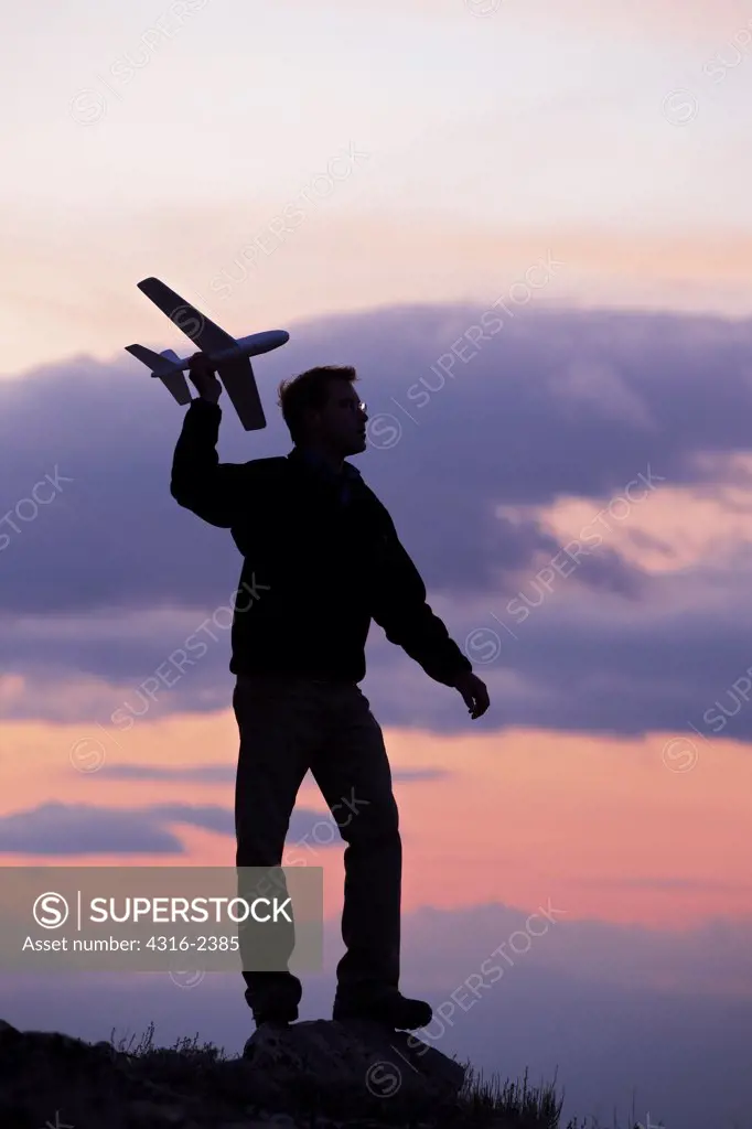 A man launches a toy foam glider at dusk.