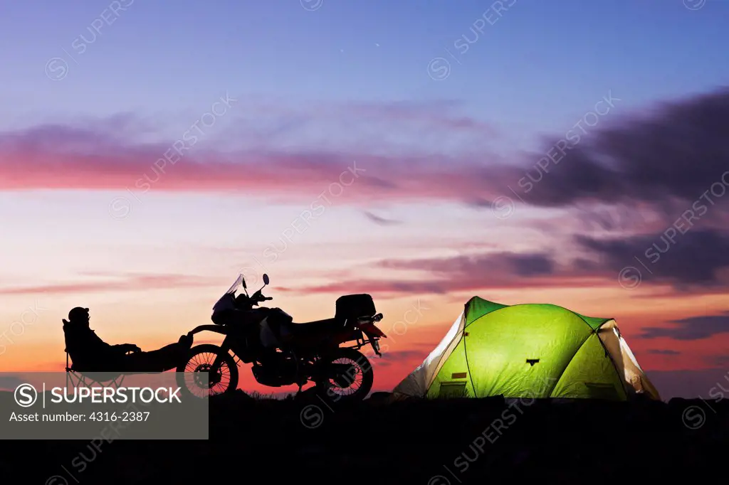 An off-road motorcyclist enjoys solitude at dusk at his camp for the night.