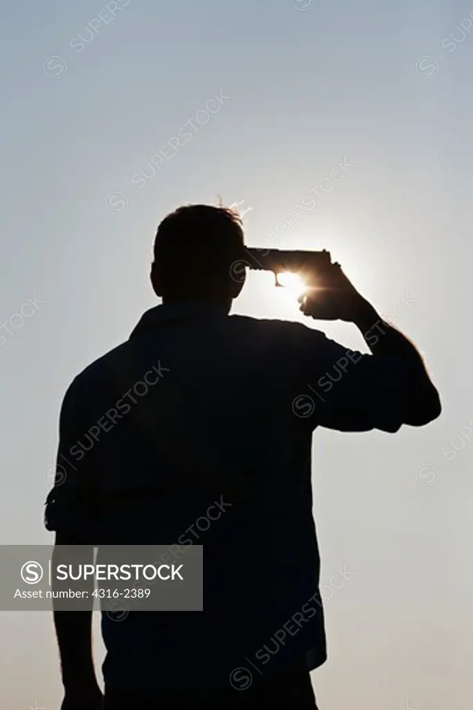 A man looking into the Sun and holding a pistol to his head as if to commit suicide.