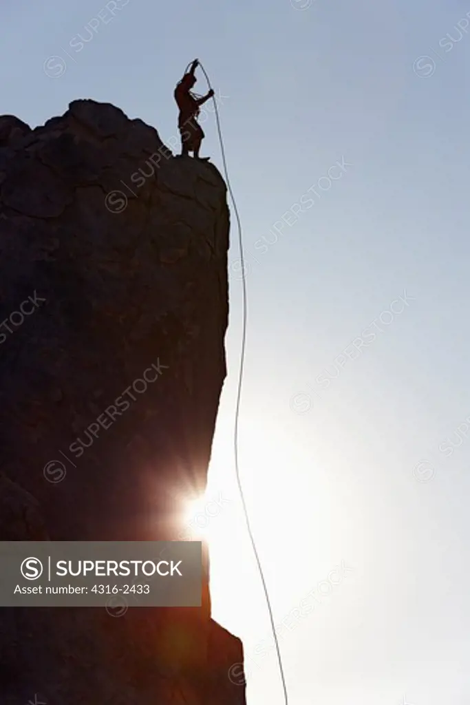 A climber prepares to rappel down an overhanging cliff face by adjusting his rope. The setting sun diffracts around the cliff face. This is in the Alabama Hills of California, below Mount Whitney in the Sierra Nevada Mountains near the town of Lone Pine.