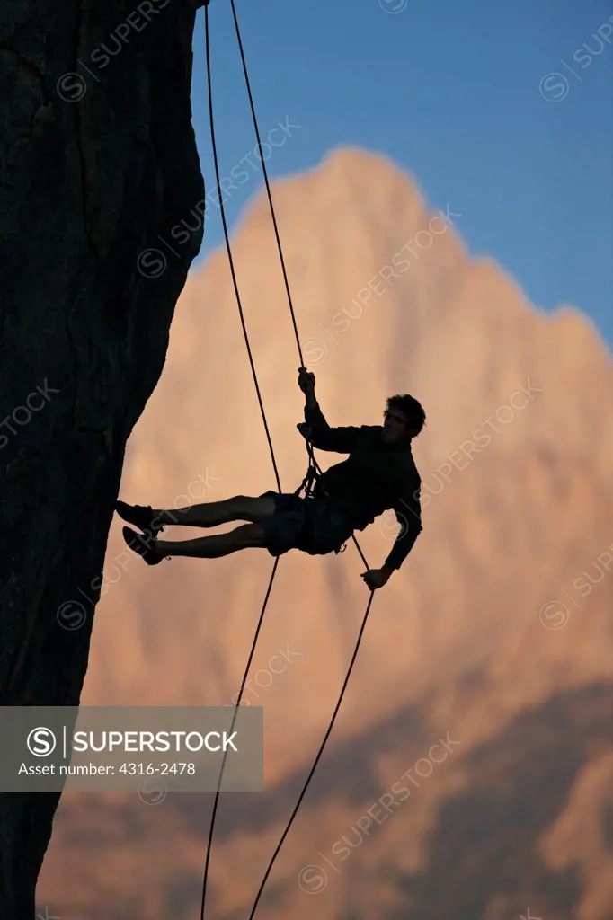 A climber rappels off of a cliff silhouetted against Mount Whitney in California's eastern high Sierra Nevada mountains. The climber is in the Alabama Hills, near the town of Lone Pine.
