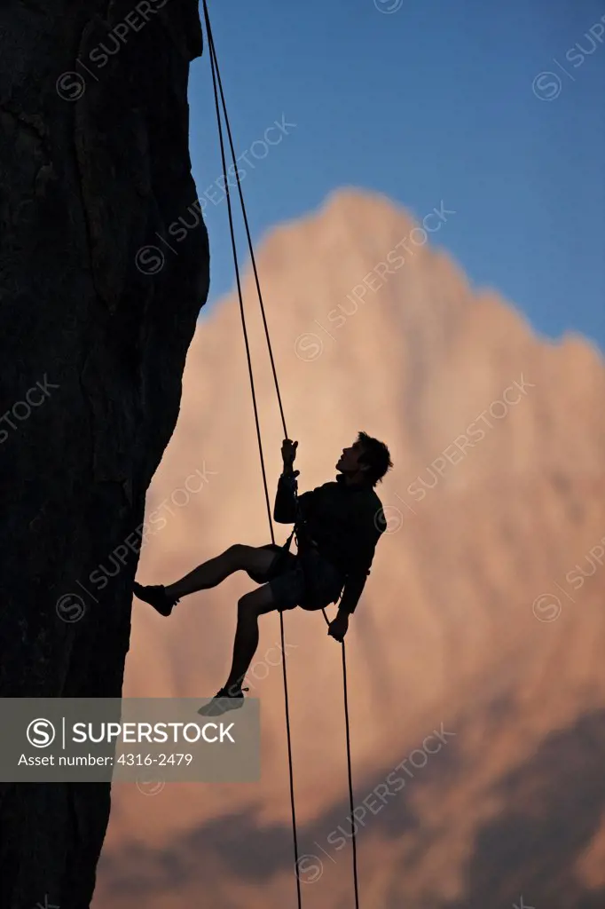 A climber rappels off of a cliff silhouetted against Mount Whitney in California's eastern high Sierra Nevada mountains. The climber is in the Alabama Hills, near the town of Lone Pine.
