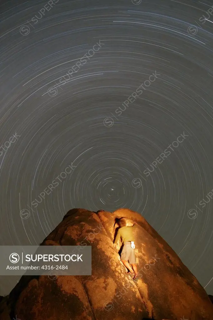 A climber ascends a boulder in the Alabama Hills of California, near the town of Lone Pine, into a 'vortex' of stars. The center star is Polaris, The North Star, and the star trail circles result from the rotation of the Earth.