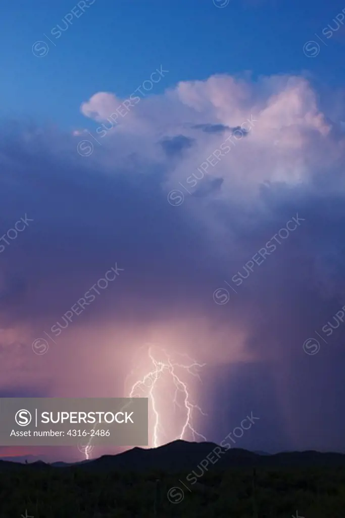 A bolt of lightning strikes the Tucson Mountains, from a thunderhead, or cumulonimbus. Sheets of rain can be seen surrounding the lightning.