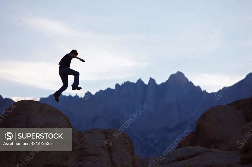 A man jumps off of a boulder in California's Alabama Hills, under Mount Whitney, At dusk. Mount Whitney, near the California town of Lone Pine, is the highest mountain in the conterminous United States, at 14,495 feet above sea level.
