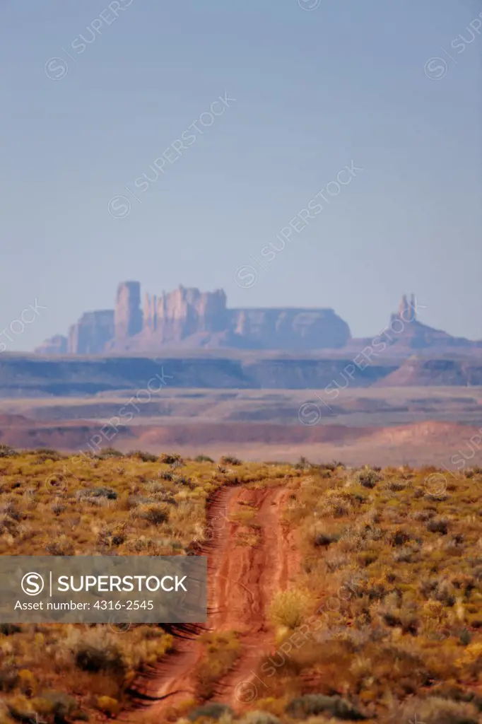 A dirt road in Utah's Valley of the Gods with Monument Valley in the background.