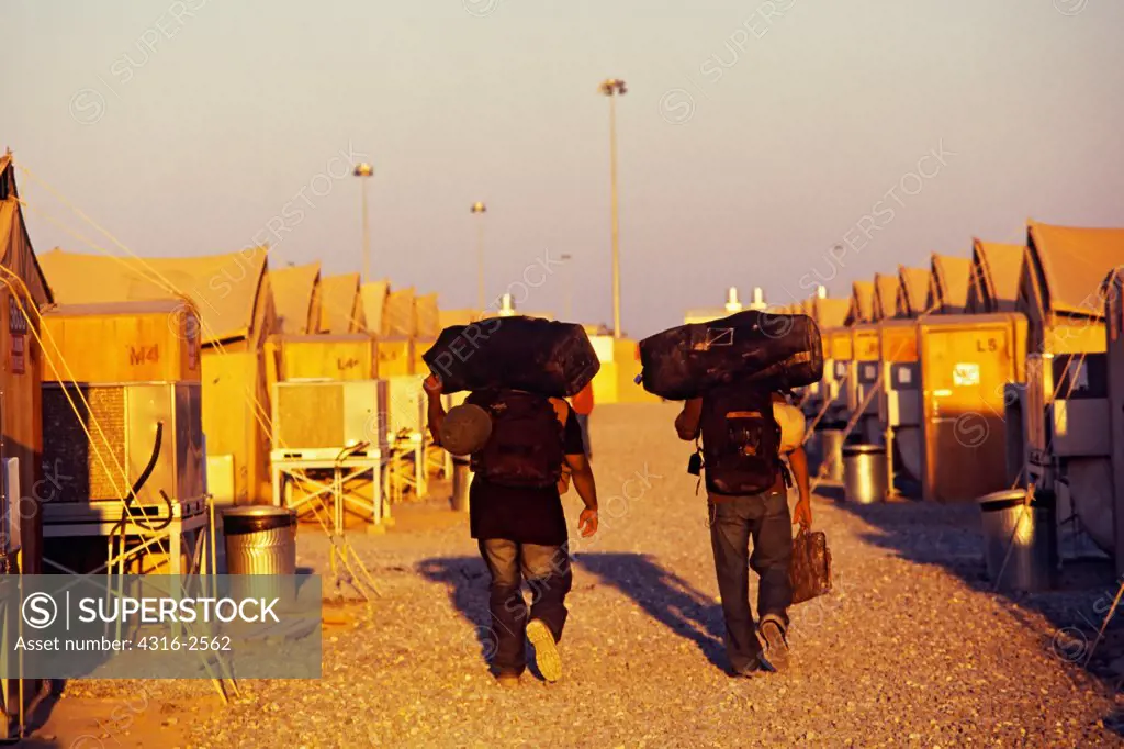 Two men carry their belongings in a tent city at an undisclosed base in Kuwait, on their way back to the United States from the war in Iraq.