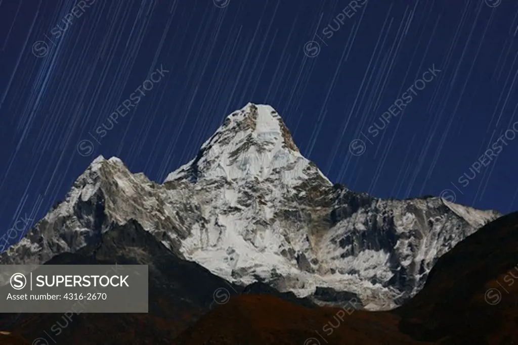Nighttime view of Ama Dablam in moonlight, with star trails in the night sky.