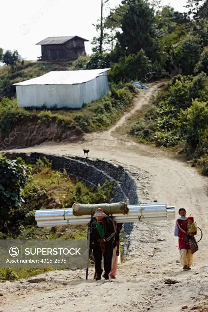 A Nepalese man and woman carry construction supplies down a dirt road.