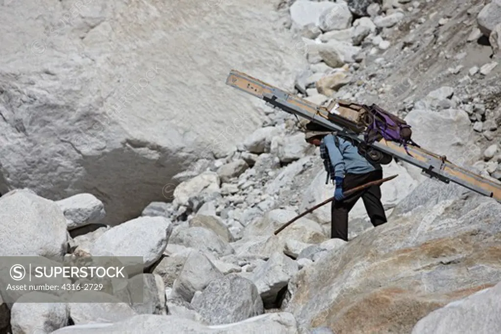 A Nepalese porter hunches over under the weight of an extremely heavy load as he ascends slopes under Mount Everest.