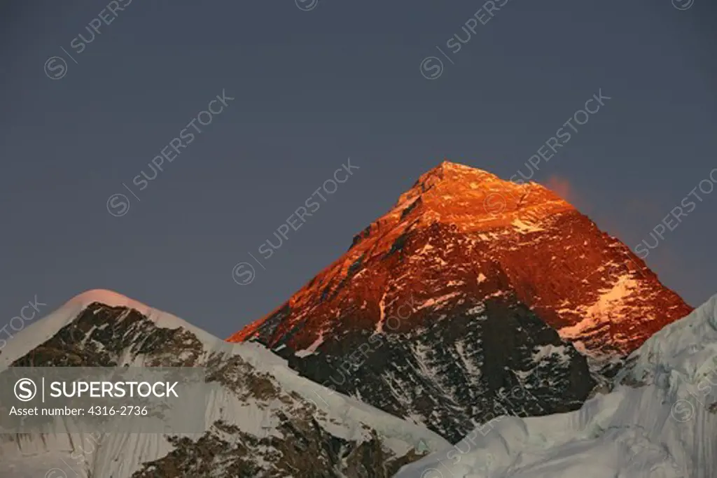 The last of the day's sunlight casts a brilliant orange and red alpenglow  on the summit pyramid of Mount Everest, Nepal.