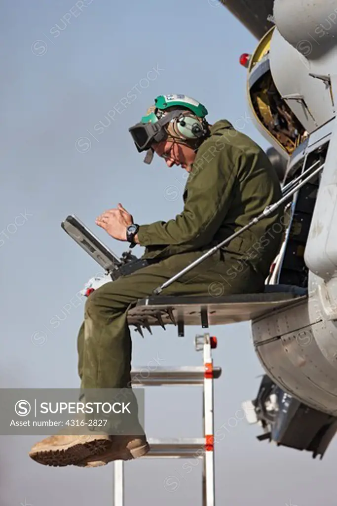A U.S. Marine aircraft maintainer consults a laptop computer during maintenance on one of the two engines of a MV-22 Osprey.