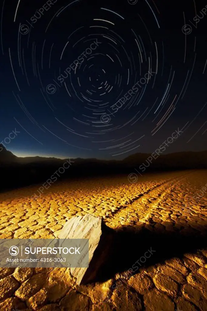 A composite image showing a swirl of stars above Racetrack Playa and one of the playa's famous moving rocks on the dry lake surface. The 'sailing stones' have never been filmed in motion, and there are several theories on how they move. Wind and ice are thought to be the major factors. A stone may move only once in two or three years, developing a track that can last three to four years.