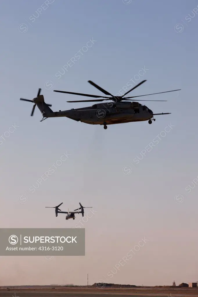 A hovering U.S. Marine Corps CH-53E and a distant MV-22 Osprey launching From Camp Bastion, Helmand Province, southern Afghanistan.