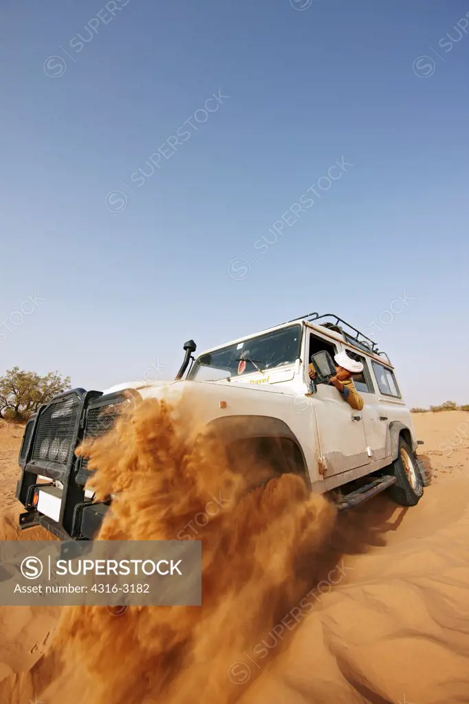 A spinning wheel of a Land Rover throws sand into the air as the driver attempts to extricate the vehicle stuck in the sand of Erg Chegaga (Chegaga Dunes), in the interior of the Sahara Desert, Morocco.