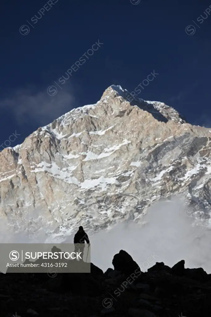 A mountain climber silhouetted by the west face of Makalu at sunset. The climber is at Makalu Base Camp, in the Mount Everest Region. Makalu is the fifth highest mountain in the world.
