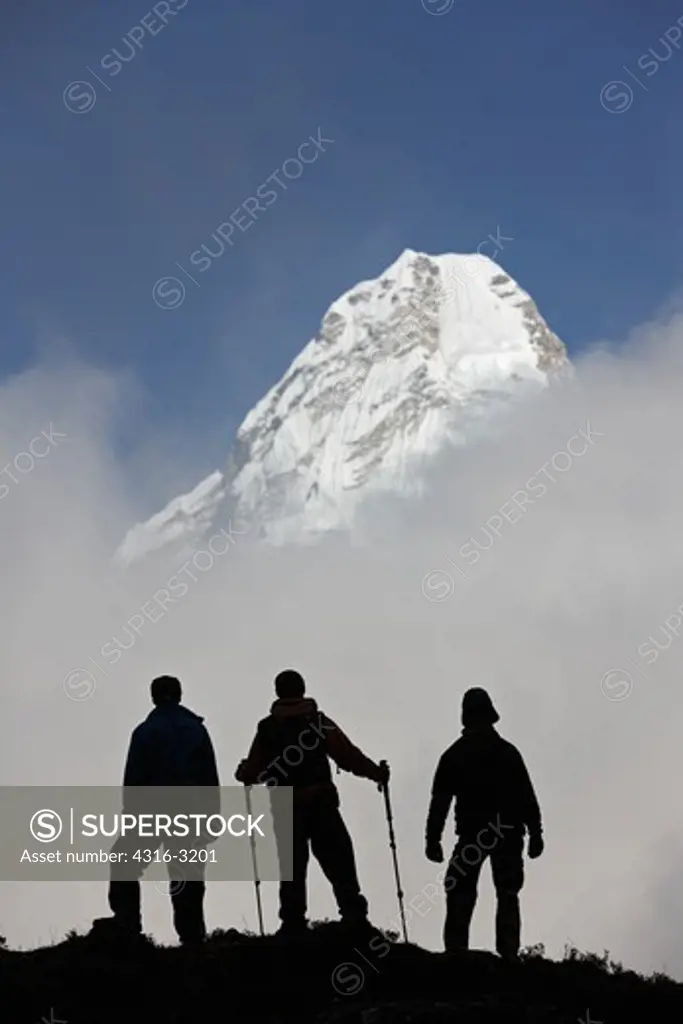 Nepali porters silhouetted by storm clouds and Ama Dablam, Nepal.