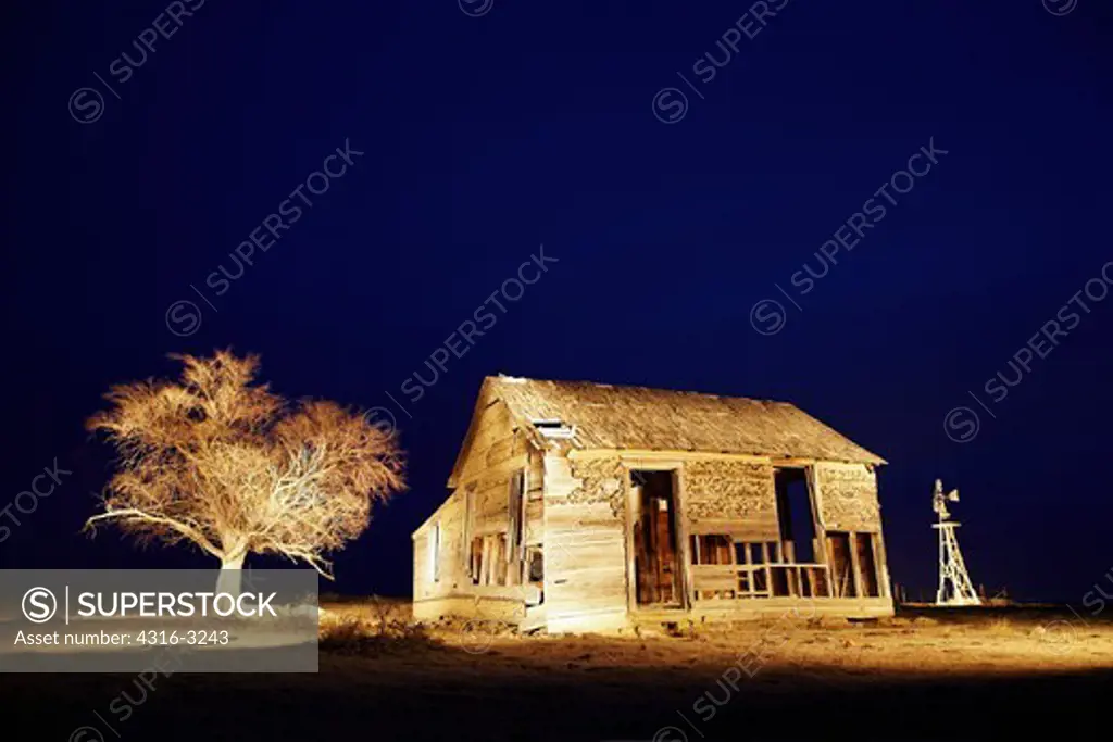 A night view of a decaying farm house, an old  Fairbanks-Morse Eclipse windmill, and a dead tree, on eastern Colorado's plains.