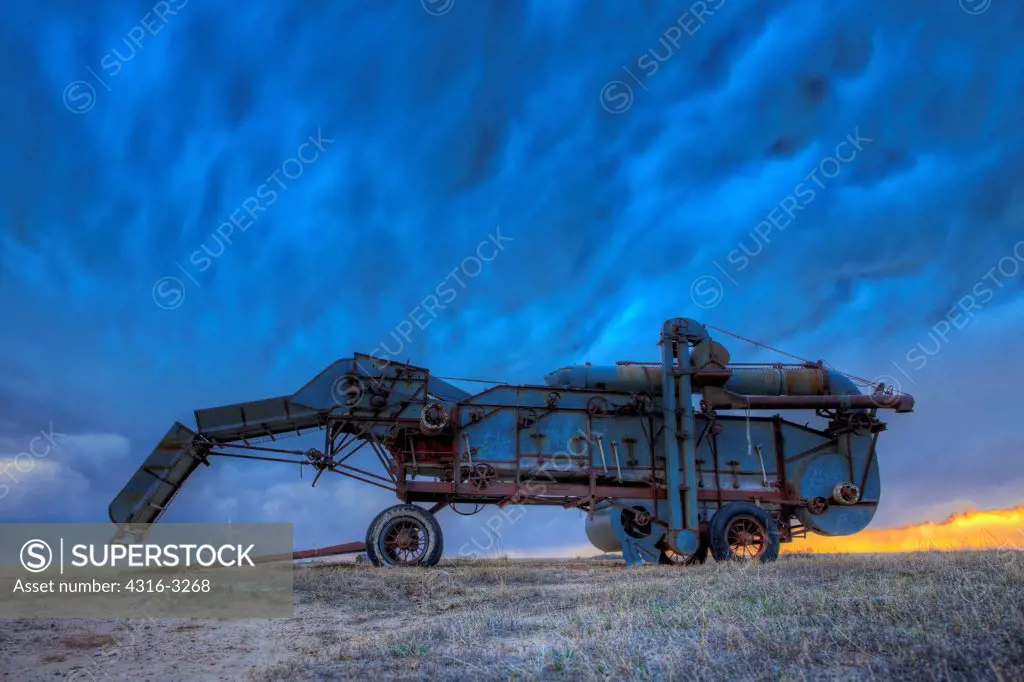 A 1930s era McCormick-Deering threshing machine, also called a thresher, under storm clouds on Colorado's Eastern Plains, in a High Dynamic Range (HDR) Image.