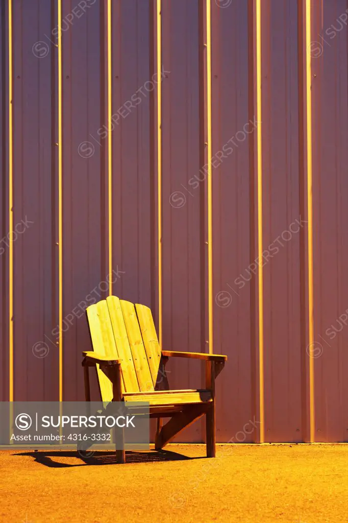 An Adirondack chair with a backdrop of an aluminum building (an airplane hanger) with parallel structural ribs.