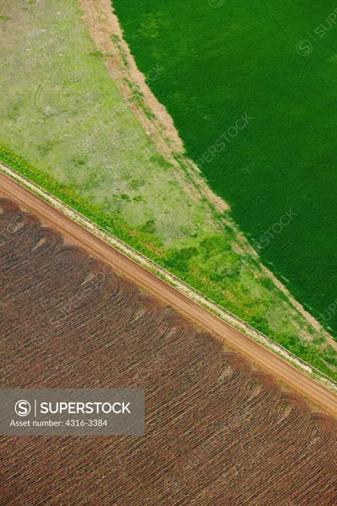 An aerial view of farm land on the plains of eastern Colorado. Three fields intersect, a round green irrigated field rolls next to a triangle of lighter land, and brown plowed land separated by an irrigation ditch.