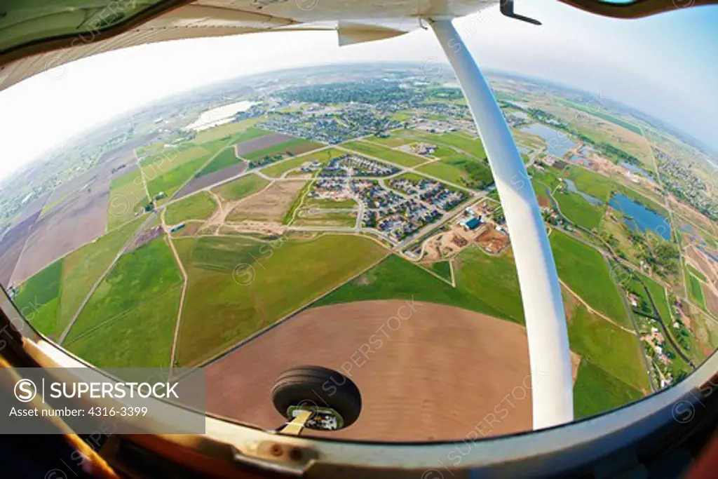 An aerial fisheye view of farm land and landing gear and wing of a light aircraft in northern Colorado.