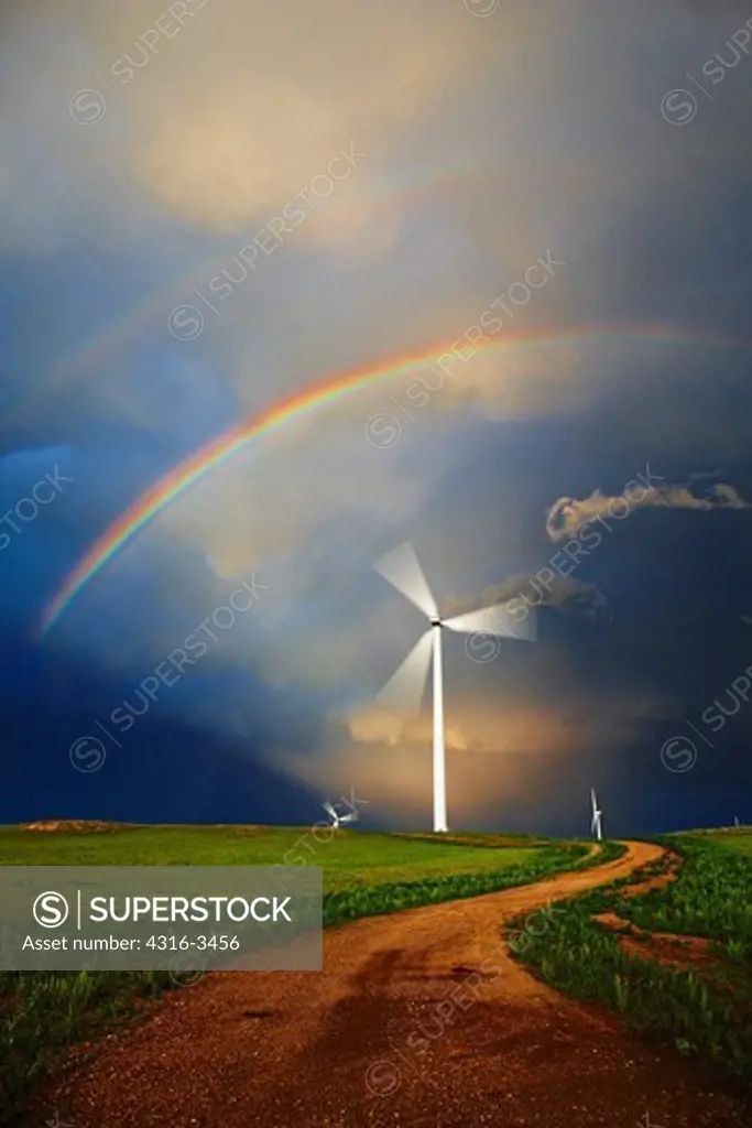 Winding road below spinning wind turbine and double rainbow.