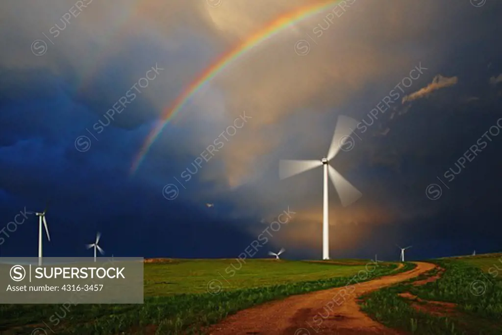 Winding road below spinning wind turbine and double rainbow.