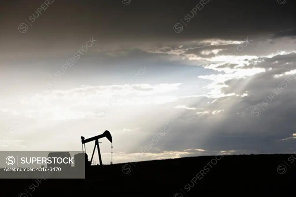 Oil well pump jack silhouetted by crepuscular rays.