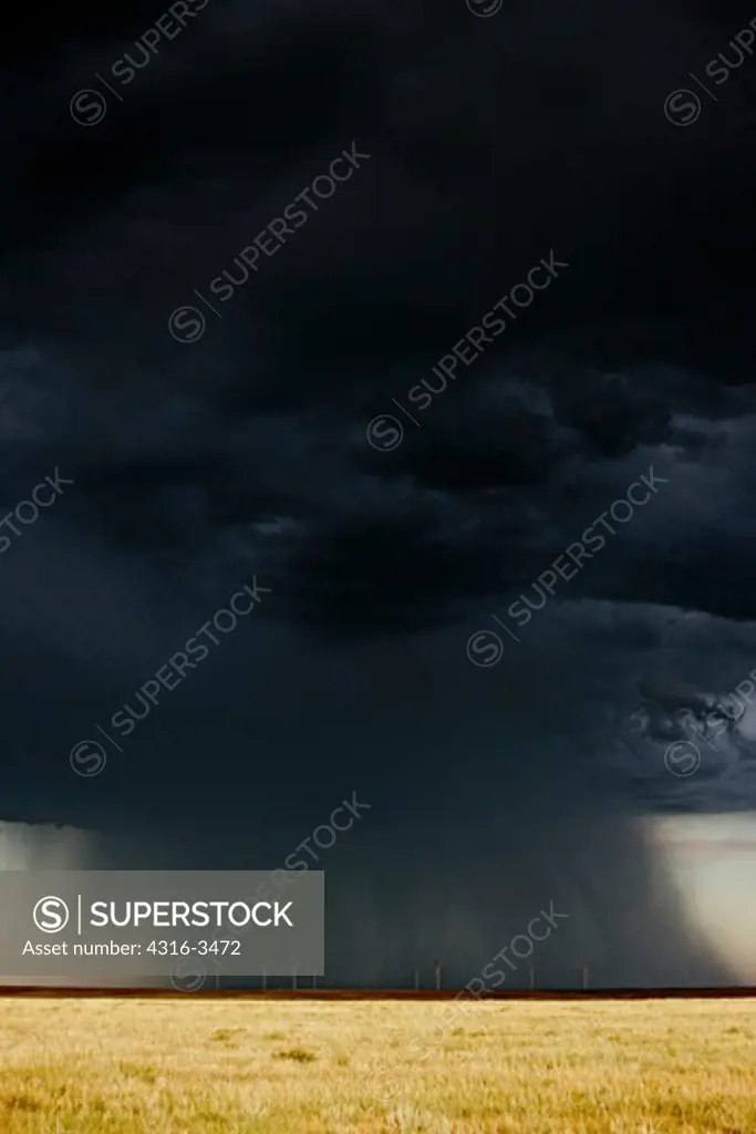 Dark curtains of rain from a large, powerful thunderstorm dwarf a line of electricity generating wind turbines.