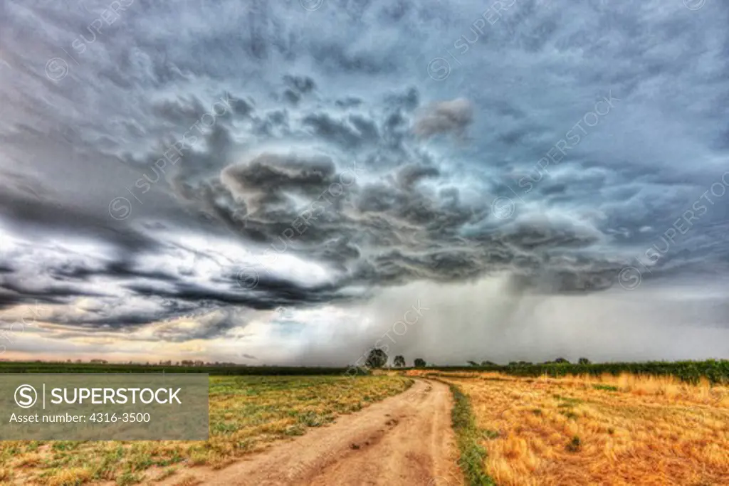 Lone dirt road winding toward approaching storm, high dynamic range, or HDR image.