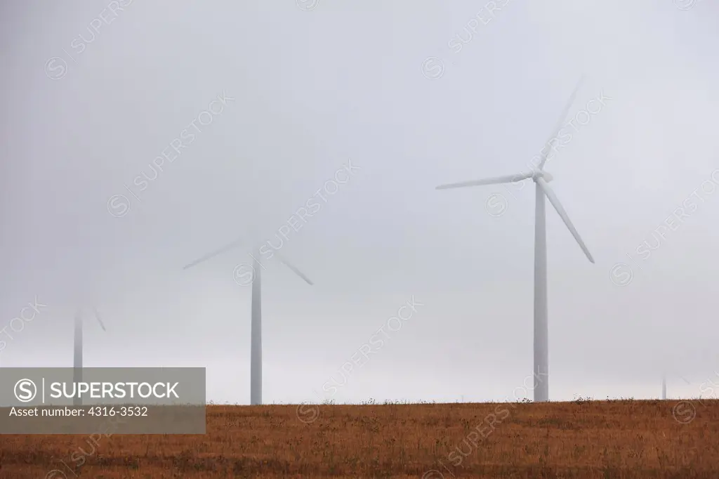 Wind turbines partially shrouded by a cloud.