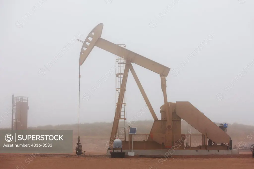 Oil well pump jack shrouded by a low hanging cloud.