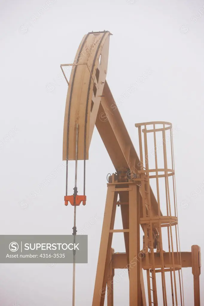 Oil well pump jack shrouded by a low hanging cloud.