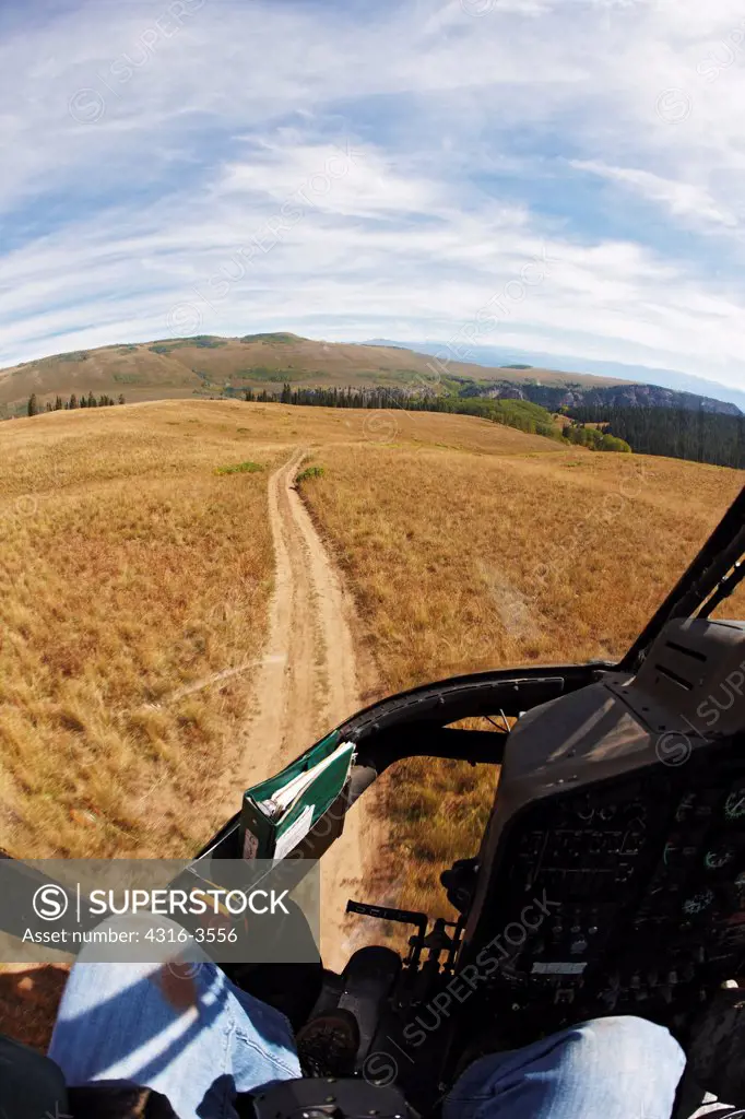 View of a dirt road high in Colorado's Rocky Mountains from cockpit of a Bell OH-58 Kiowa helicopter.