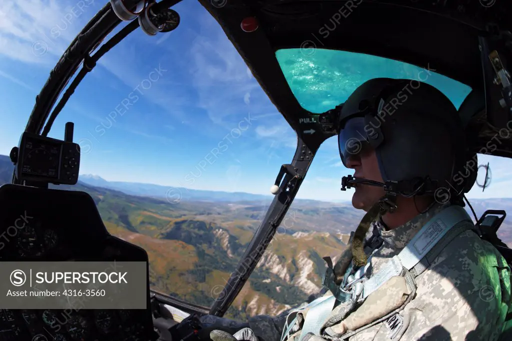 Cockpit view of a pilot of a Bell OH-58 Kiowa while flying above a deep canyon in Colorado's Rocky Mountains.