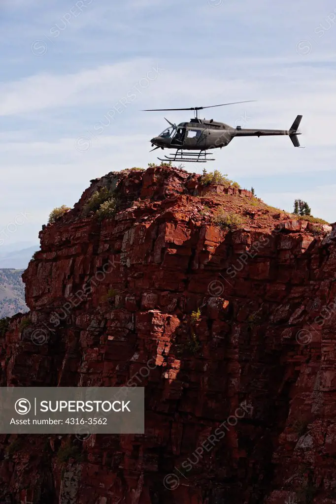 A Bell OH-58 Kiowa hovers just above a steep cliff high in Colorado's Rocky Mountains.