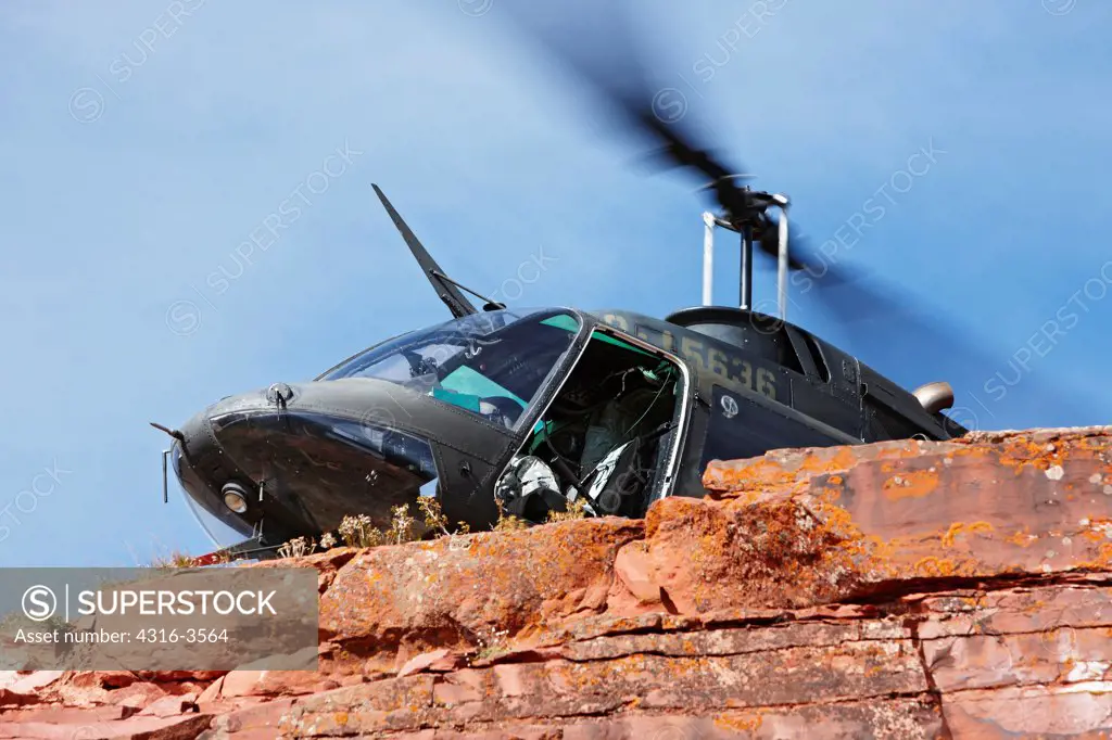 A Bell OH-58 Kiowa hovers just behind a steep cliff high in Colorado's Rocky Mountains.