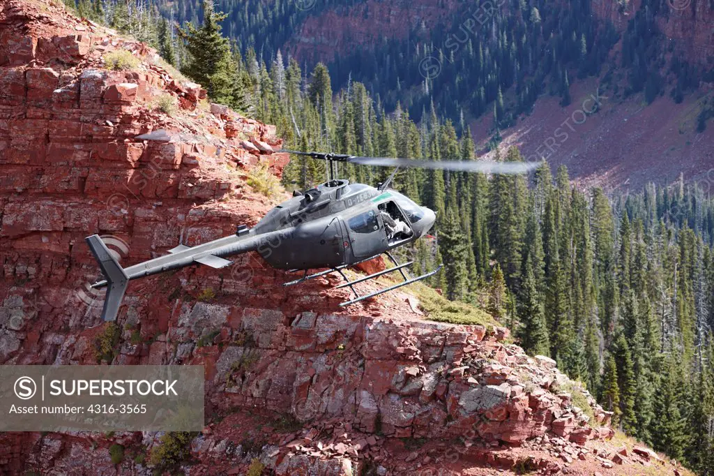 A Bell OH-58 Kiowa hovers just above a steep cliff high in Colorado's Rocky Mountains.