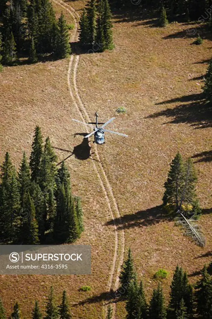 Air to air view of a Sikorsky UH-60 Blackhawk hovering above a two-track dirt road high in Colorado's Rocky Mountains.
