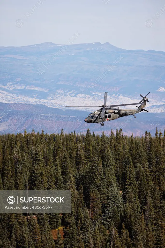Sikorsky UH-60 Blackhawk helicopter above trees in Colorado's Rocky Mountains.