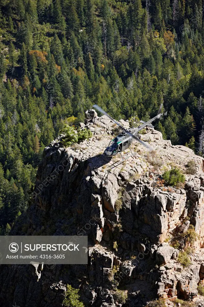 An OH-58 Kiowa idles after landing atop a rock spire in a deep canyon in Colorado's Rocky Mountains.