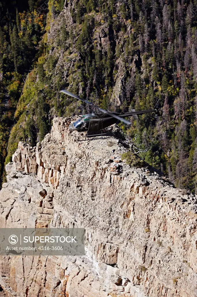An OH-58 Kiowa idles after landing atop a rock spire in a deep canyon in Colorado's Rocky Mountains.